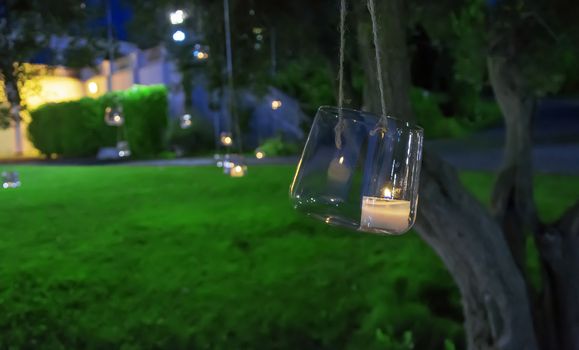 candle in a glass hanging from a tree in a formal garden