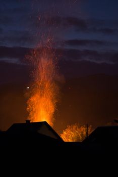 House in flames, fire just starting, nighttime and reflections of fire seen on nearby trees, emergency services haven't yet responded