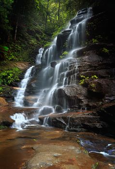 The beautiful and tranquil flowing water down the rocks with lush green foliage all about.  Sylvia Falls Valley of the Waters in Wentworth Falls,  Blue Mountains Australia