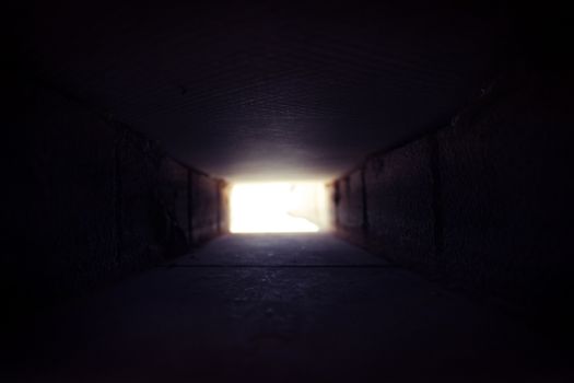 Dark square tunnel made of concrete. At the end of there is a very bright light.
