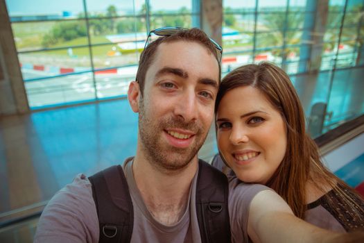 Happy couple taking selfie with smartphone or camera in airport.