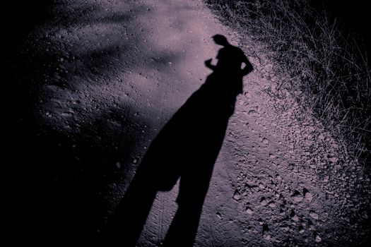 Elongated shadow of a man on gravel. A surreal ambiance in black and purple.
