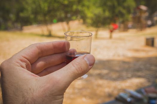 Man hand holding a shot glass with red wine at a social meeting outdoor.