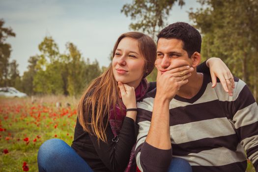 Young couple looking away with a thoughtful look while sitting on the grass in a field of red poppies.