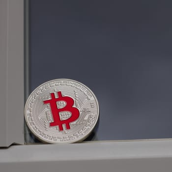Digital currency physical silver bitcoin coin with red sign on the window in England.