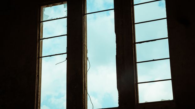 Broken window in an abandoned building - View from inside - sky with clouds seen through the window.