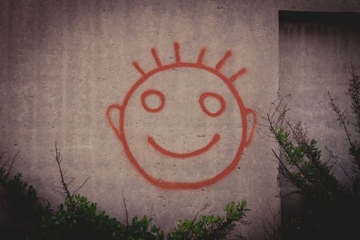 Graffiti painting of red happy smiley face on a concrete wall.
