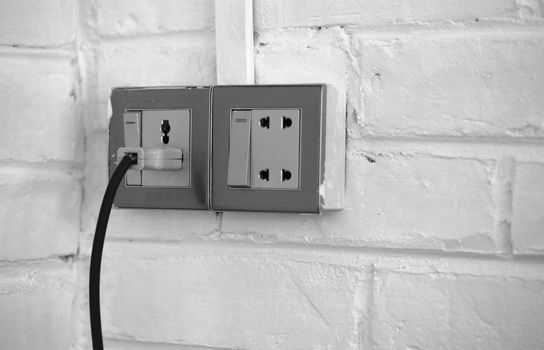 BLACK AND WHITE PHOTO OF PLUGGED OLD SOCKET ON WHITE BRICK WALL