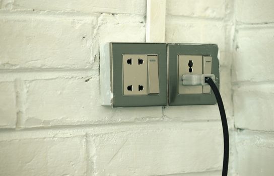 COLOR PHOTO OF PLUGGED OLD SOCKET ON WHITE BRICK WALL