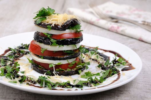 Appetizer from eggplant , slices of mozzarella combined in a pile with tomatoes spilled with herbs, seasoned   Parmesan cheese
