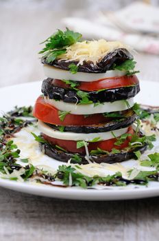 Appetizer from eggplant , slices of mozzarella combined in a pile with tomatoes spilled with herbs, seasoned   Parmesan cheese