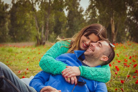 Young couple sitting on the grass in a field of red poppies and smiling and laughing at each other