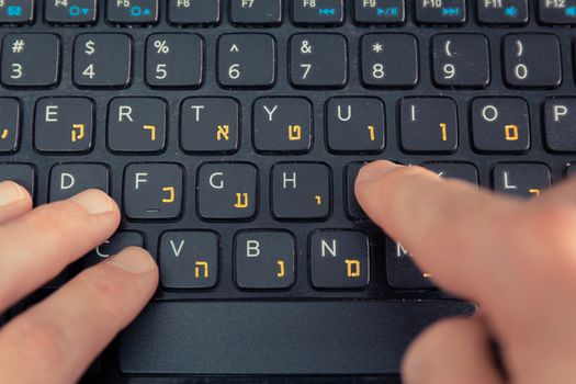 Man typing on a keyboard with letters in Hebrew and English - Laptop keyboard - Top View - Close up
