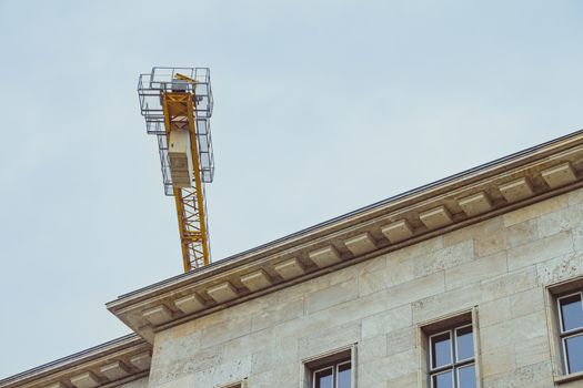 End part of yellow construction crane over roof of office building.