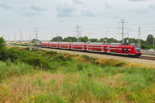 Red israeli passenger train in motion out of the city near Highway 4.