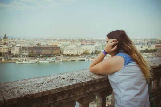 Woman leans on the railing and watching the horizon while Budapest cityscape in background.