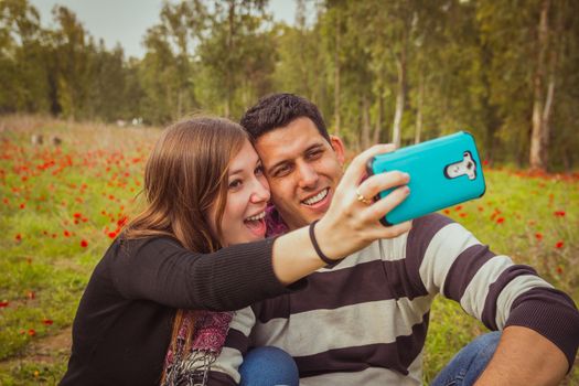 Couple taking selfie picture with their mobile phone in field of red poppies.