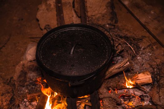 Cooking meal in cauldron on burning campfire at night.