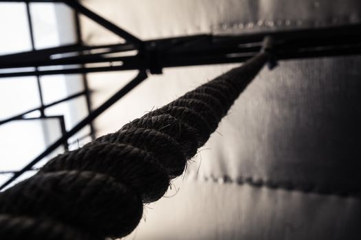 Brown climbing rope hanging from roof - Close up view from below - Black and white silhouette
