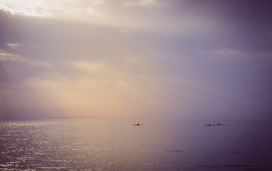 Three canoes sailing at sea during sunset.

