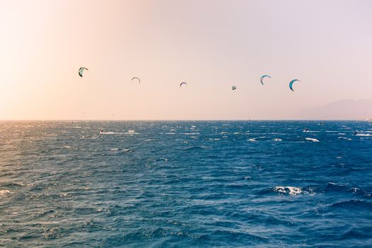 Windsurfers sailing in the Red Sea.
Near the beach of Eilat, Israel.
Bright orange light coming from the sun on the left.
