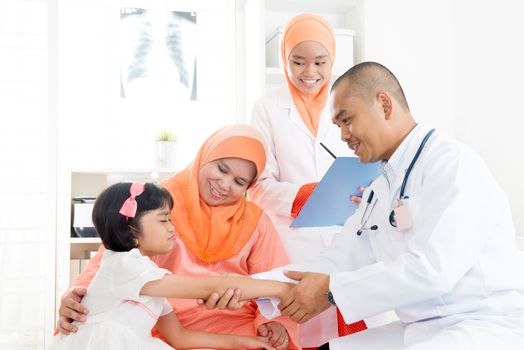 Southeast Asian kid patient consulting medical doctor. Muslim family. Little girl with broken arm doing health check.