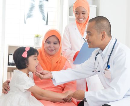 Southeast Asian male doctor examining little girl patient. Muslim medical concept.