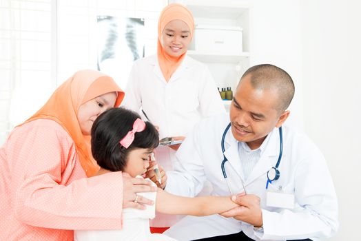 Southeast Asian doctor give injection of vaccine to girl's arm. Muslim family.
