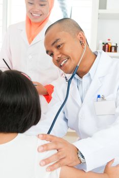 Asian children's doctor exams child with stethoscope.