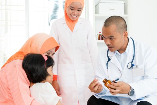 Pediatrician giving medicine to little girl at hospital. Southeast Asian Muslim family.