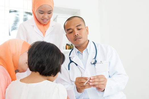 Doctor checking little girl's temperature at hospital.  Southeast Asian Muslim family.