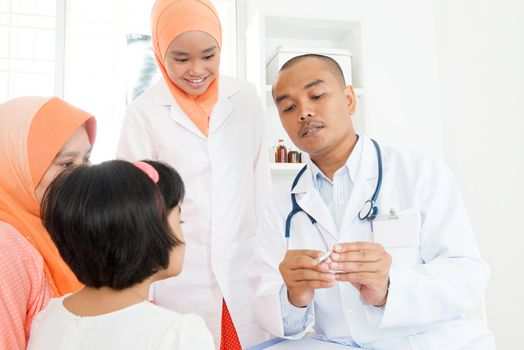 Pediatrician checking temperature of sick patient at hospital.  Southeast Asian Muslim family.