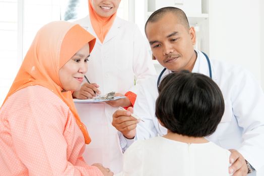 Doctor checking children temperature at hospital.  Southeast Asian Muslim family.