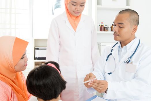 Doctor checking girl temperature at hospital.  Southeast Asian Muslim family.