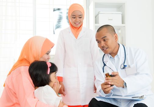 Asian male doctor explaining medicine usage to little patient's parent. Family medical concept.