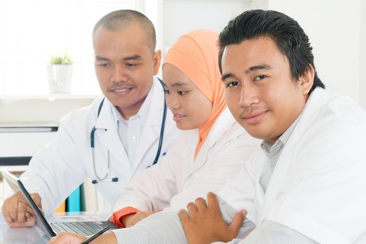 Medical team using a laptop in a bright office. Southeast Asian Muslim doctors and nurses.