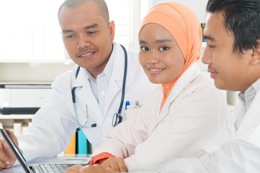 Medical colleagues discussing and working with laptop in the hospital. Southeast Asian Muslim doctors and nurses.