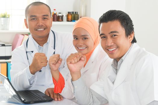 Successful medical doctors celebrating success inside hospital room. Southeast Asian Muslim people.