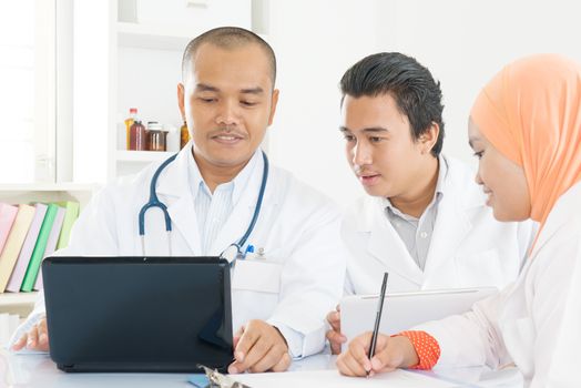 Hospital, medical education, health care, people and medicine concept - group of happy doctors with tablet pc and computers meeting at medical office. Southeast Asian Muslim.