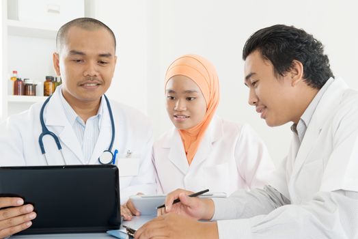 Group of doctors discuss at meeting in hospital office. Southeast Asian Muslim medical people.