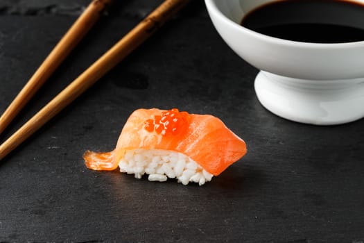 Salmon Nigiri with salmon roe on black slate stone with chopsticks and bowl of soy sauce. Raw fish in traditional Japanese sushi style. Horizontal image.