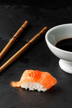 Salmon Nigiri with salmon roe on black slate stone with chopsticks and bowl of soy sauce. Raw fish in traditional Japanese sushi style. Vertical image.