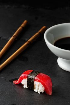 Red tuna Nigiri with Nori seaweedi on black slate stone with chopsticks and bowl of soy sauce. Raw fish in traditional Japanese sushi style. Vertical image.