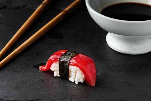 Red tuna Nigiri with Nori seaweedi on black slate stone with chopsticks and bowl of soy sauce. Raw fish in traditional Japanese sushi style. Horizontal image.
