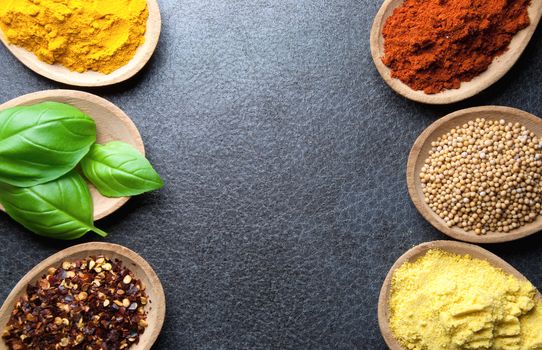 Closeup of herbs and spices in wooden spoons on a kitchen worktop background