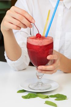 Closeup shot of cherry smoothie in a big glass cup with two straws in woman's hands. Lady with a drink