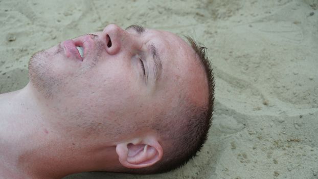 a young man lies on the sand on the beach.