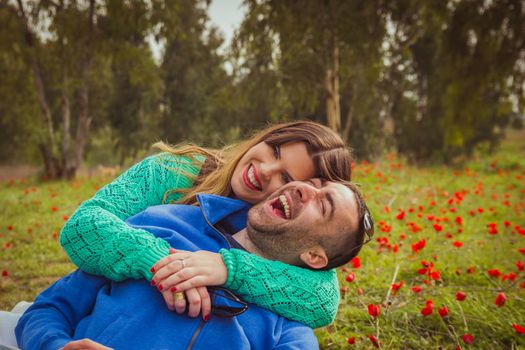 Young couple sitting on the grass in a field of red poppies and smiling and laughing at each other