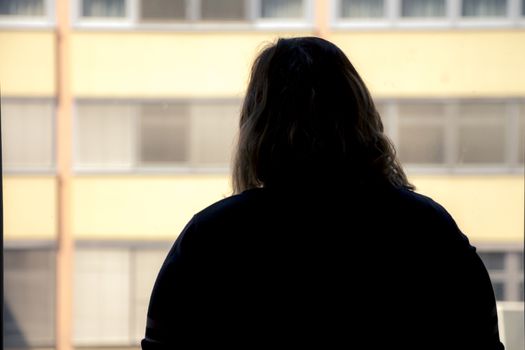 Back view of silhouette of a woman putting on makeup in front of a window.