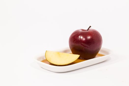 Red apple and red apple slice on white plate with honey isolated on a white background. Symbols of Jewish New Year - Rosh Hashanah.  